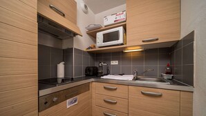 A compact kitchen with wooden cabinets, a microwave, a kettle, and a sink. - Studio in France with Mountain Views & Pool (Allos)