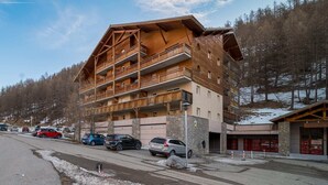A multi-story hotel with balconies, a parking area, and a ski resort in the background. - Studio in France with Mountain Views & Pool (Allos)