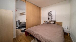 A bedroom with a bed, a gray sofa, a wooden wardrobe, and a wall-mounted artwork of a wolf. - Studio in France with Mountain Views & Pool (Allos)
