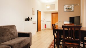 A living room with a sofa, a dining table with chairs, a television, and a kitchen area in the background. - Casa di Ziva in Rome (Rome)