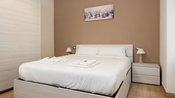 A neatly made bed with white linens and towels, a bedside table with a lamp, and a wall-mounted painting of potted plants. - Casa di Ziva in Rome (Rome)