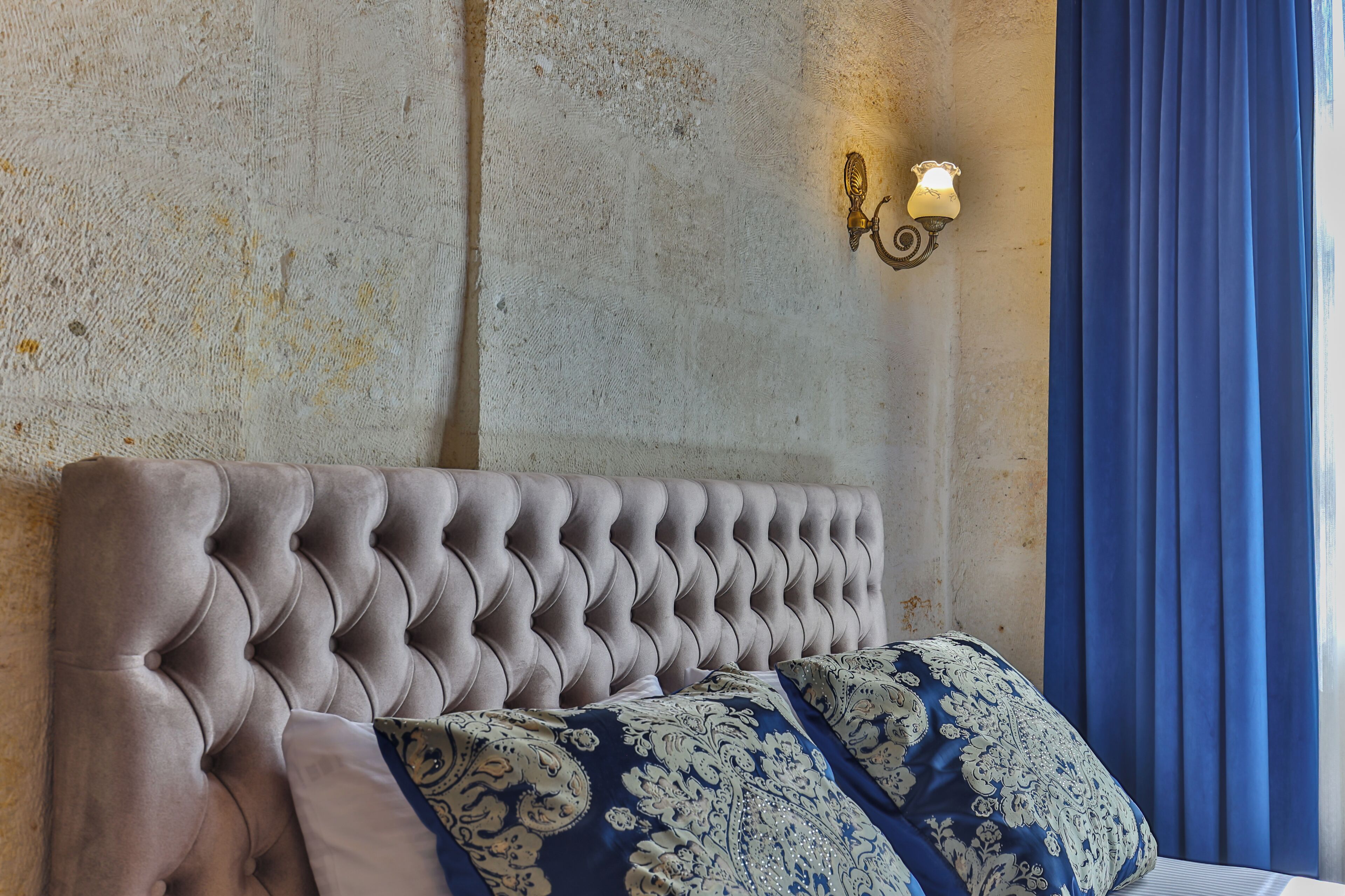 Una habitación con cabecera capitonada, almohadas estampadas, pared texturizada e iluminación instalada en la pared.