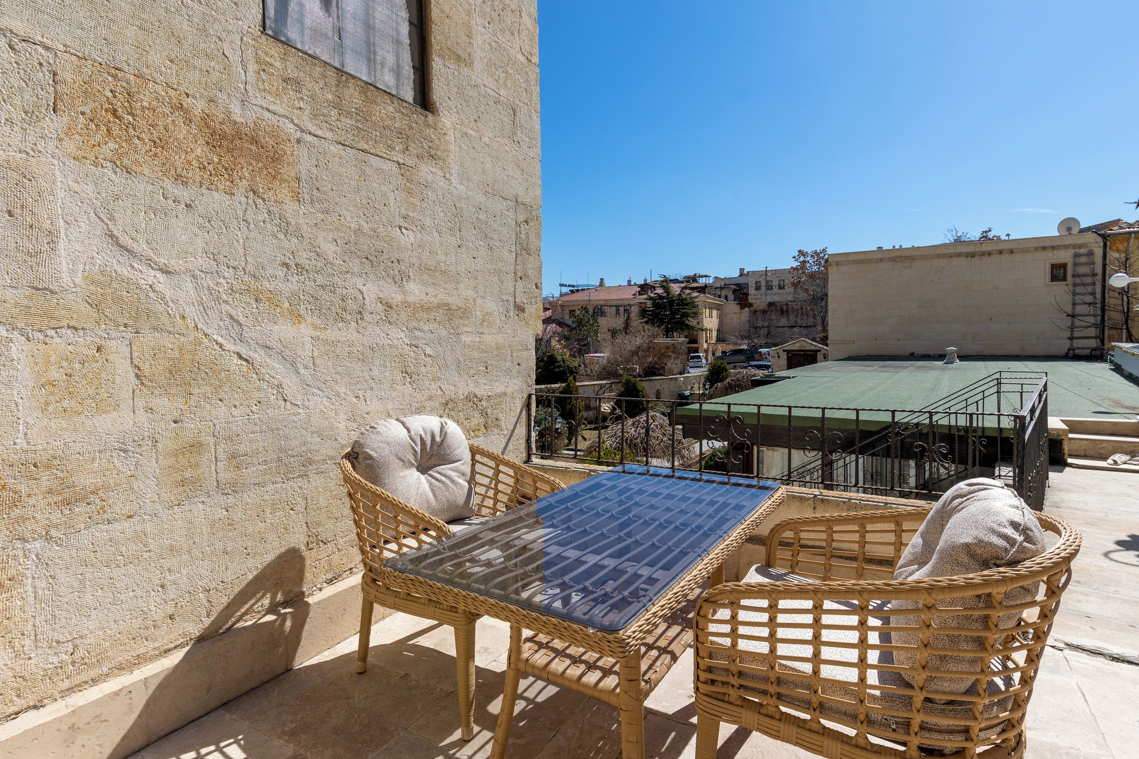 A rooftop terrace with wicker furniture and a glass table, overlooking a cityscape.