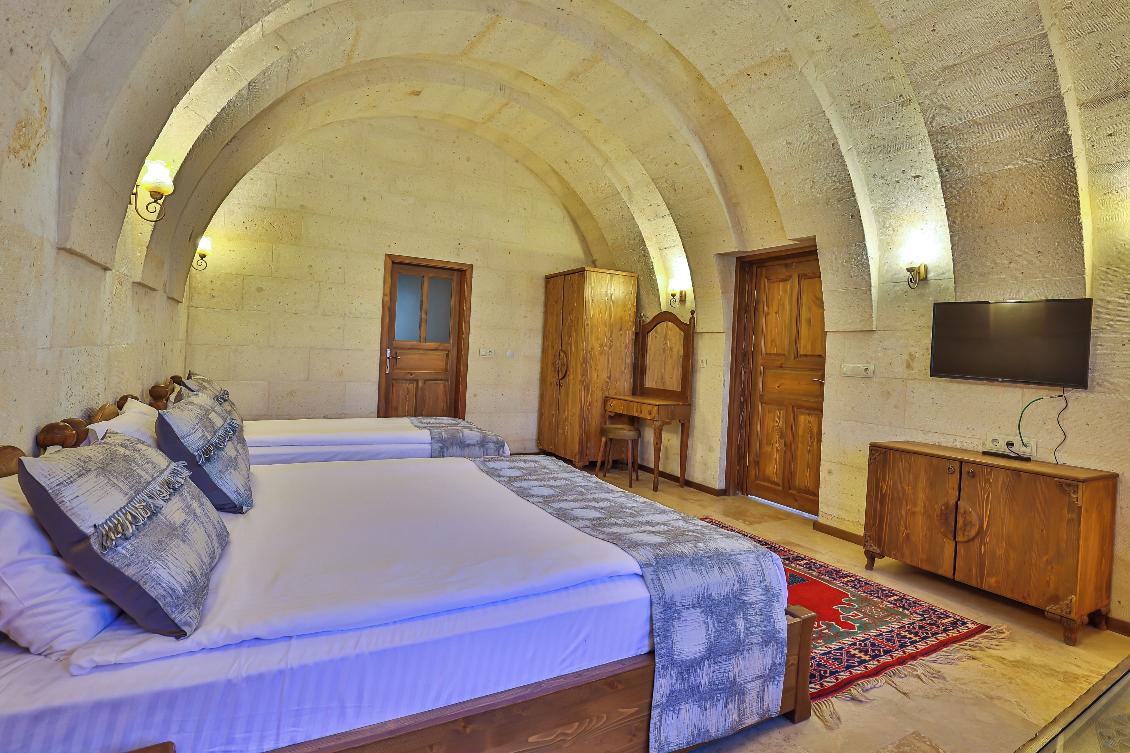 A bedroom with two beds, wooden furniture, a TV, and a stone ceiling.