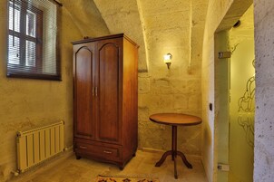 A room with a wooden wardrobe, a small round table, a radiator, and a wall-mounted light fixture.