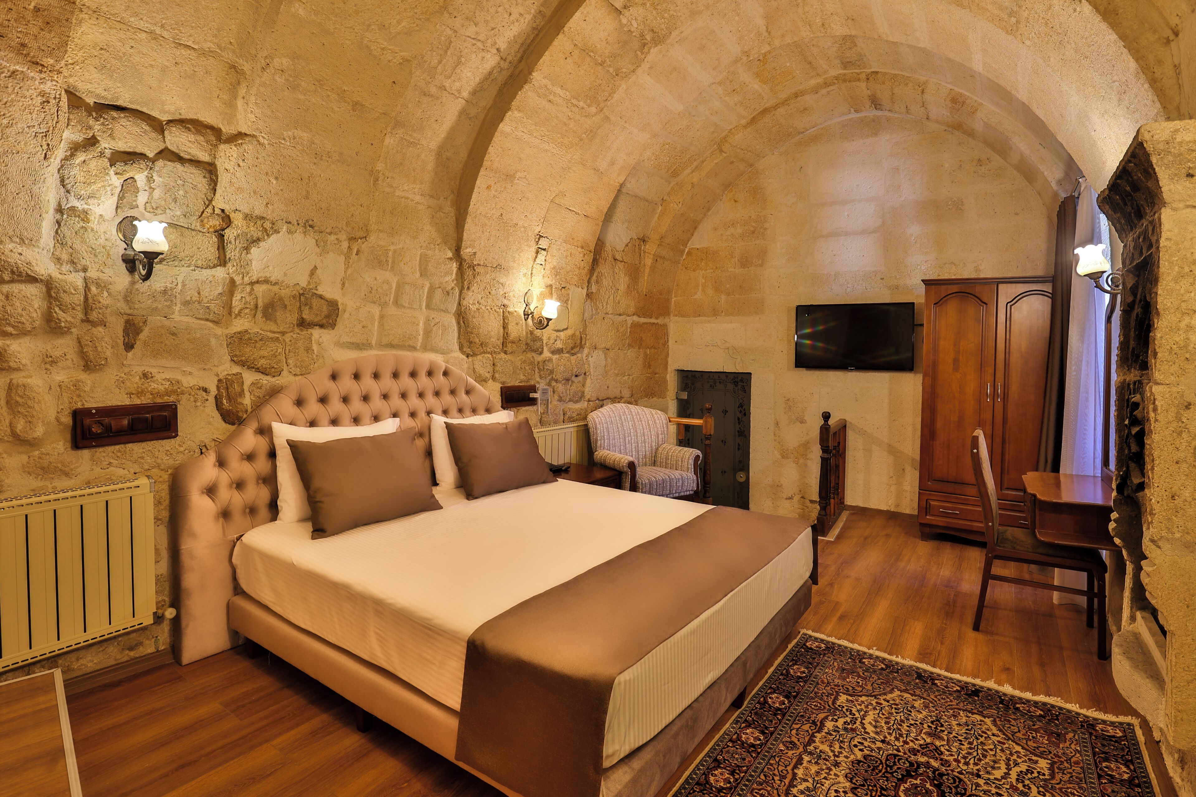 Un dormitorio con una cama grande, paredes de piedra, un escritorio de madera y un televisor.