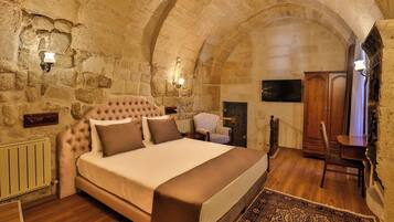 Un dormitorio con una cama grande, paredes de piedra, un escritorio de madera y un televisor.