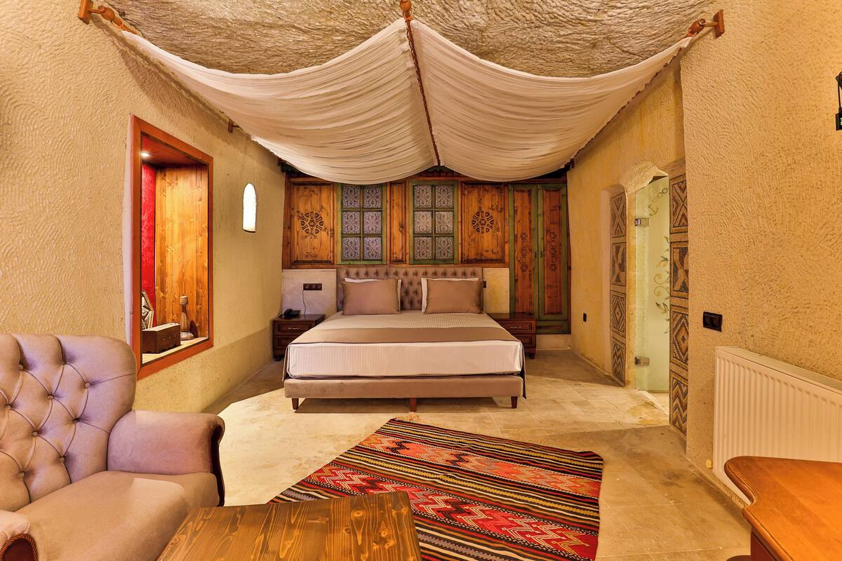 Quarto com cama grande, uma cadeira, mesa de madeira e tapete estampado.