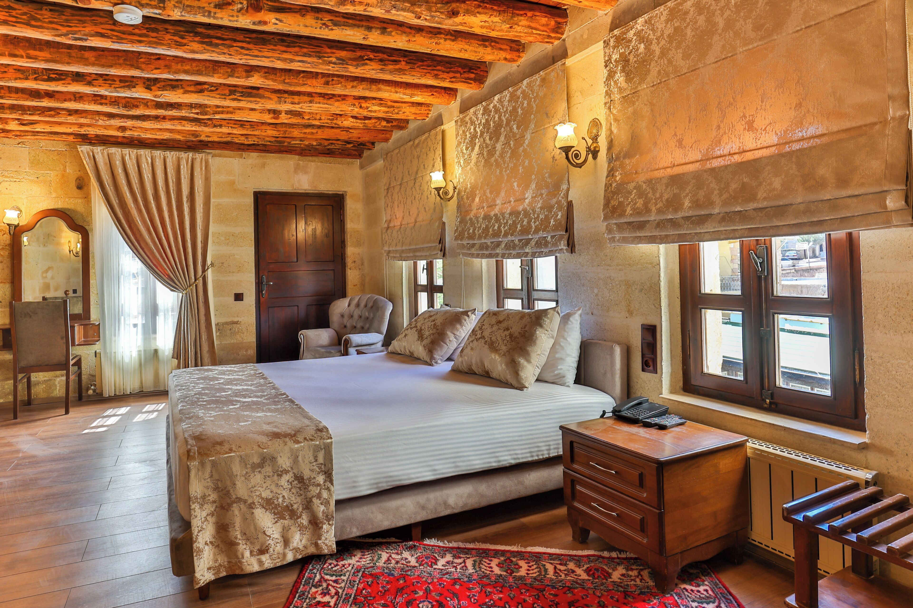 A bedroom with a wooden ceiling, a large bed with pillows, a desk, and a chair.