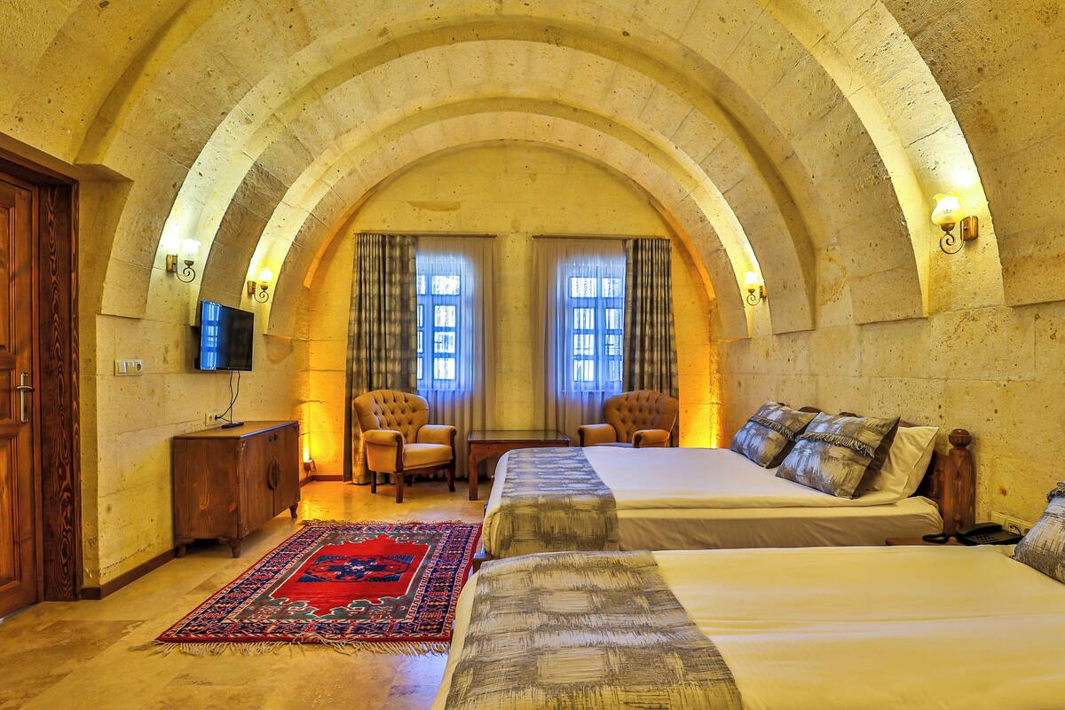 Quarto com duas camas, um armário de madeira, uma televisão e um tapete vermelho estampado.