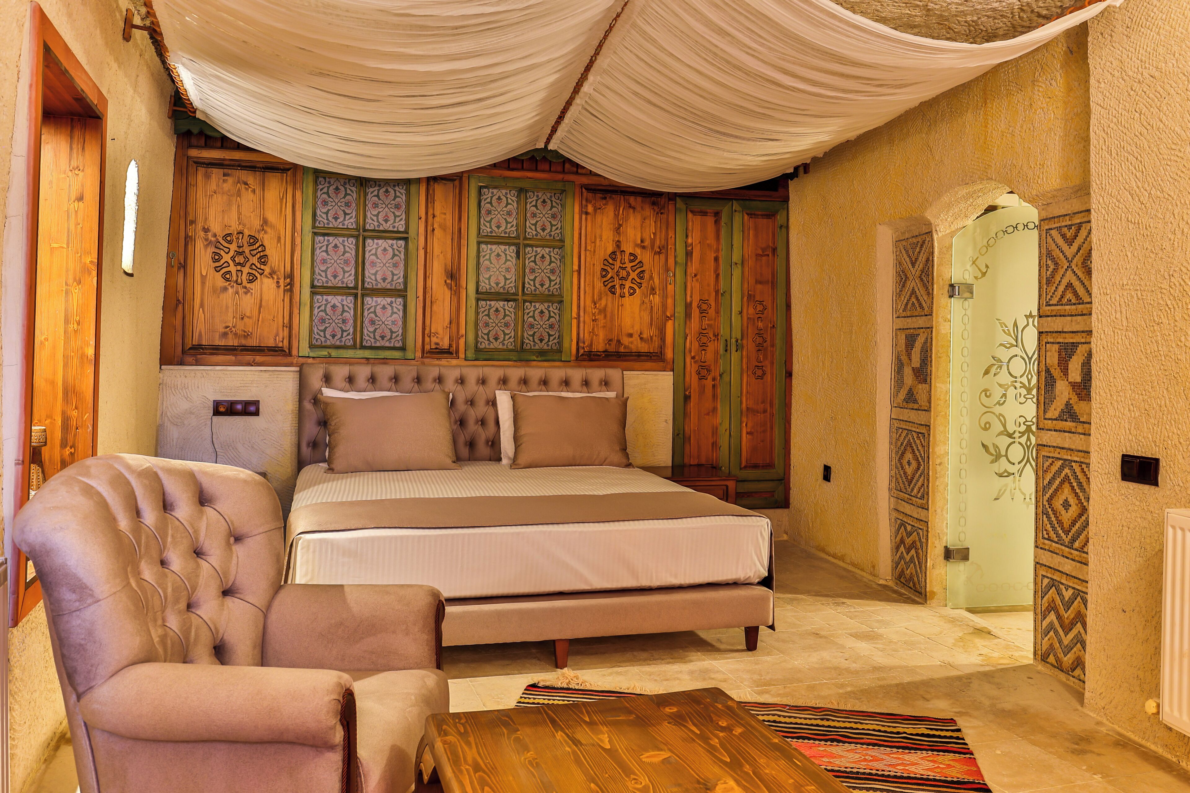 A bedroom with a large bed, a tufted armchair, and a wooden coffee table.
