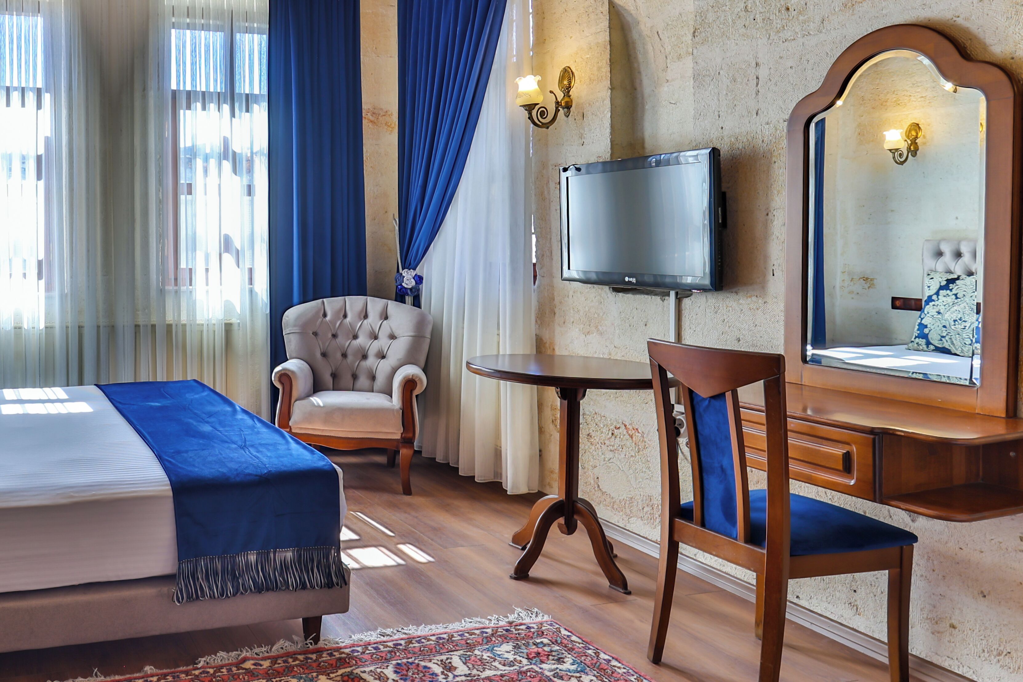 A hotel room with a bed, a chair, a small table, a TV, and a mirror.