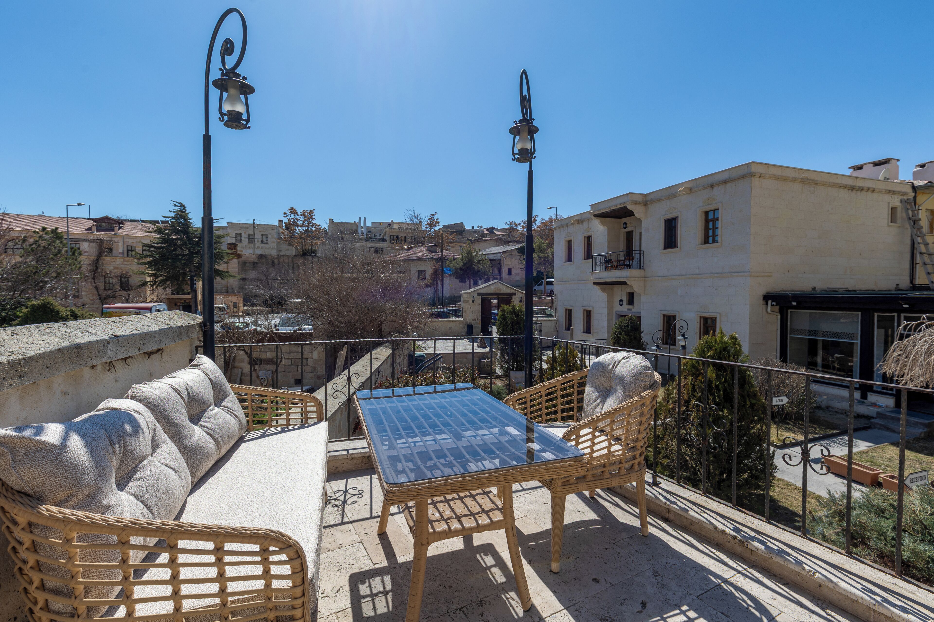 A rooftop terrace with wicker furniture, a glass table, and two street lamps.