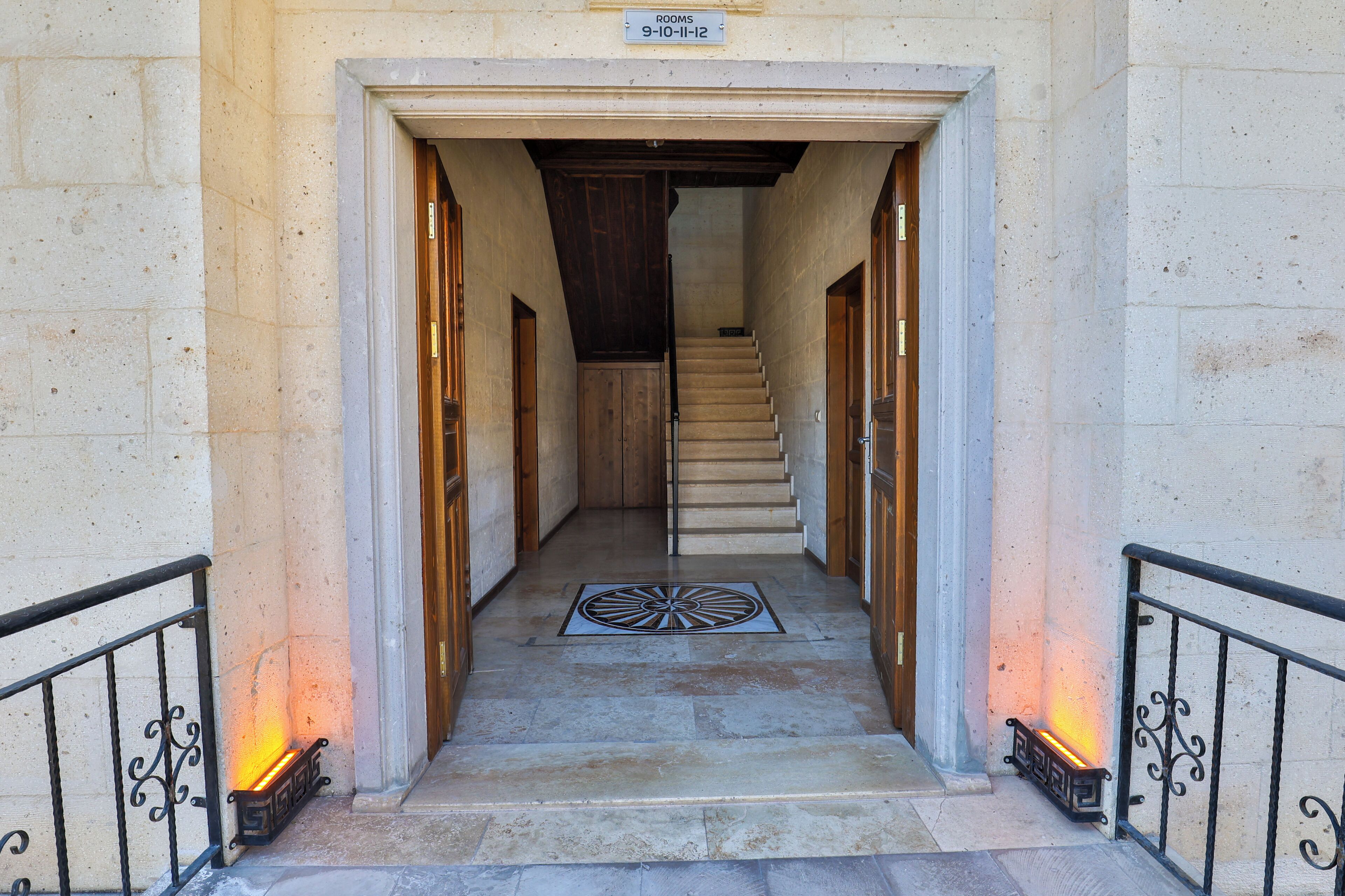 A stone-floored hallway leading to a staircase with a sign indicating room numbers 9-10-11-12.