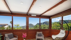 Una stanza con soffitto in legno, ampie finestre, un tavolo con un vaso di fiori e due sedie.