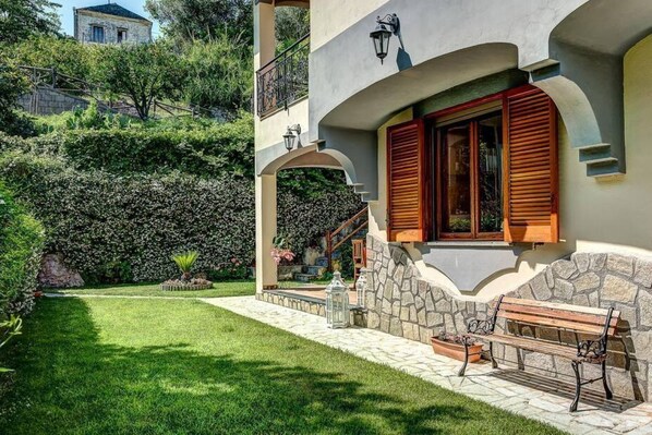 A two-story building with a stone facade, wooden shutters, and a stone bench.