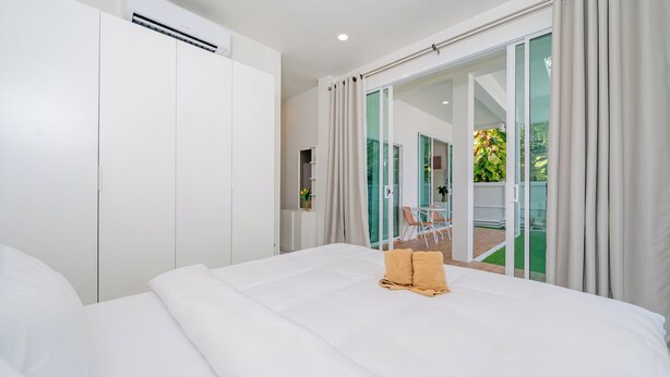 A hotel room with a large bed, a wardrobe, and a sliding glass door leading to an outdoor area. - Beachfront 2BR Pool Villa DelMar Kamala (Kamala)