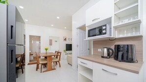 A modern kitchen with white cabinetry, a wooden dining table, and chairs. There is a microwave, a coffee maker, and a kettle on the countertop. - Beachfront 2BR Pool Villa DelMar Kamala (Kamala)