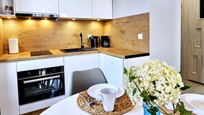 A modern kitchen with wooden cabinetry, a built-in oven, a coffee maker, and a vase of white flowers on the counter. - Apartament Loft 9 - 365PAM (Ustronie Morskie)