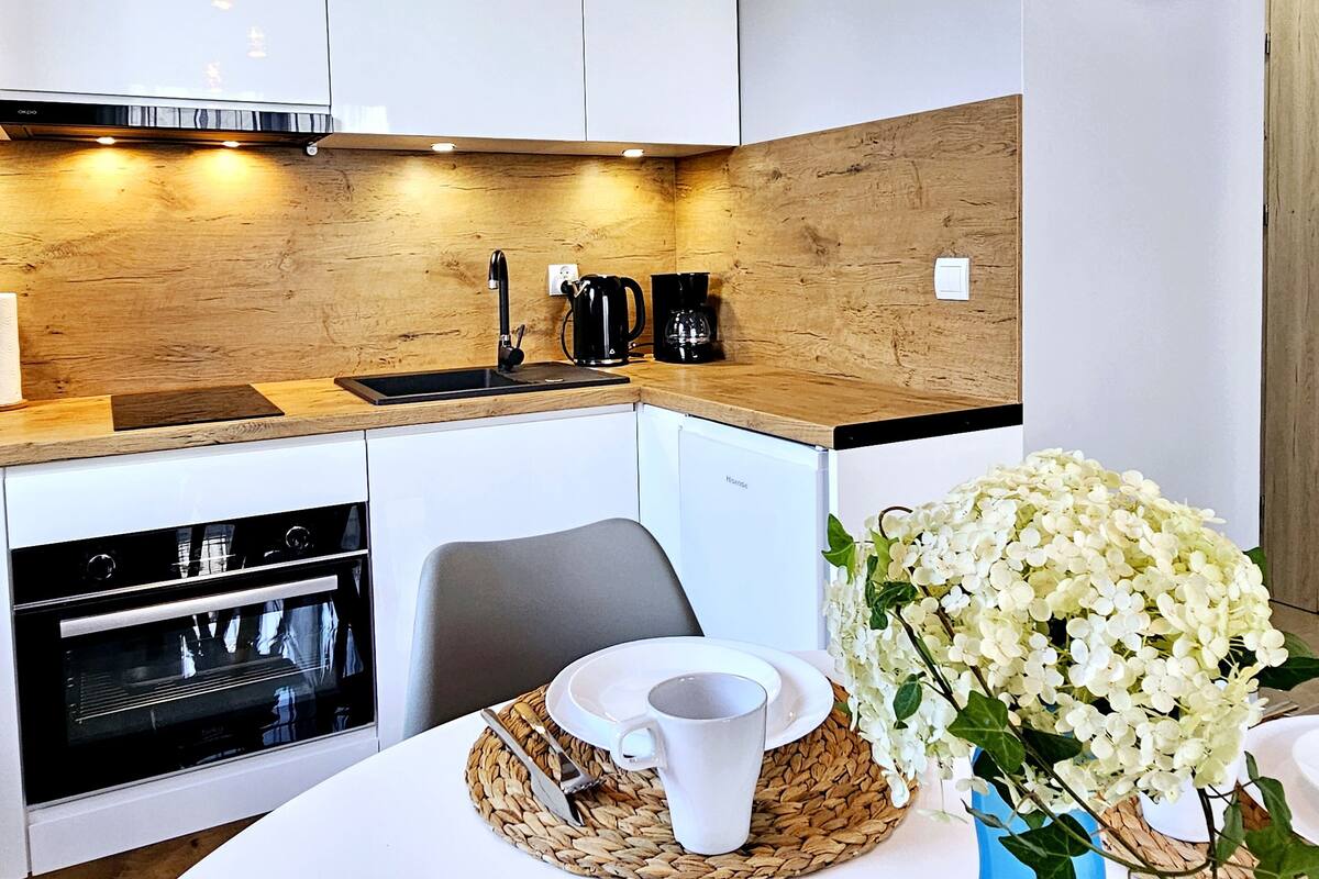 Una cocina moderna con armarios de madera, horno empotrado, cafetera y un jarrón con flores blancas en la encimera.