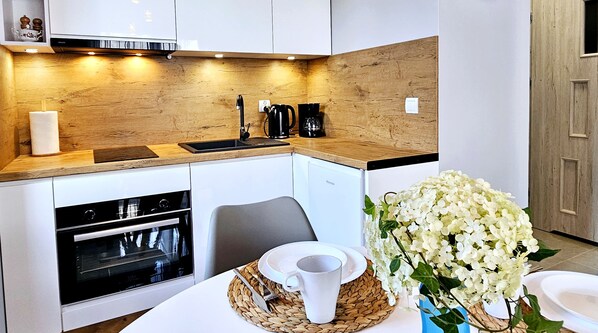 A modern kitchen with wooden cabinetry, a built-in oven, a coffee maker, and a vase of white flowers on the counter.