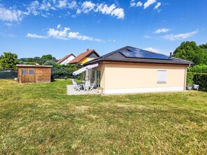 Ett enplanshus med ett sluttande tak, ett litet garage som är sammanbyggt med huset och en uteplats med utemöbler.
