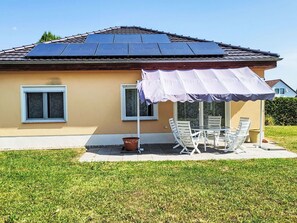 Ett hus med solpaneler på taket, en uteplats med utemöbler och en välskött gräsmatta.
