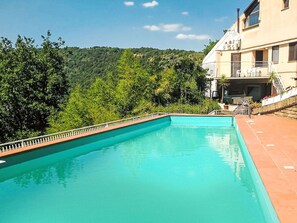Relax by the serene pool surrounded by lush greenery and a hillside backdrop.