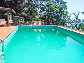 Relax by the serene pool surrounded by lush greenery and a clear sky, with a shaded seating area for a peaceful swim or afternoon by the water.