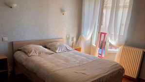 A bedroom with a wooden bed, a nightstand, a bedside lamp, and a window with curtains. - Gite LA GRANGE, in a quiet location close to Rocamadour, Padirac... (Bio)