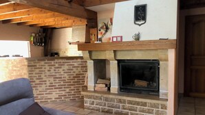 A cozy living room with a fireplace, a brick wall, and a wooden ceiling. - Gite LA GRANGE, in a quiet location close to Rocamadour, Padirac... (Bio)