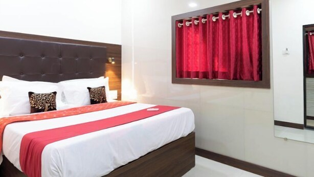 A hotel room with a large bed, red curtains, and a wooden headboard. - Hotel Nithyanand (Mumbai)