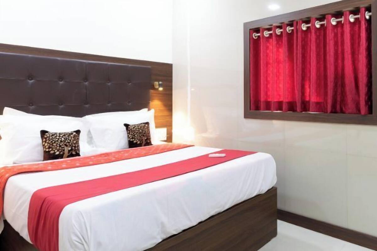 A hotel room with a large bed, red curtains, and a wooden headboard.