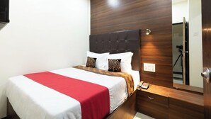 A hotel room with a bed, a nightstand, a mirror, and a wooden headboard. - Hotel Nithyanand (Mumbai)