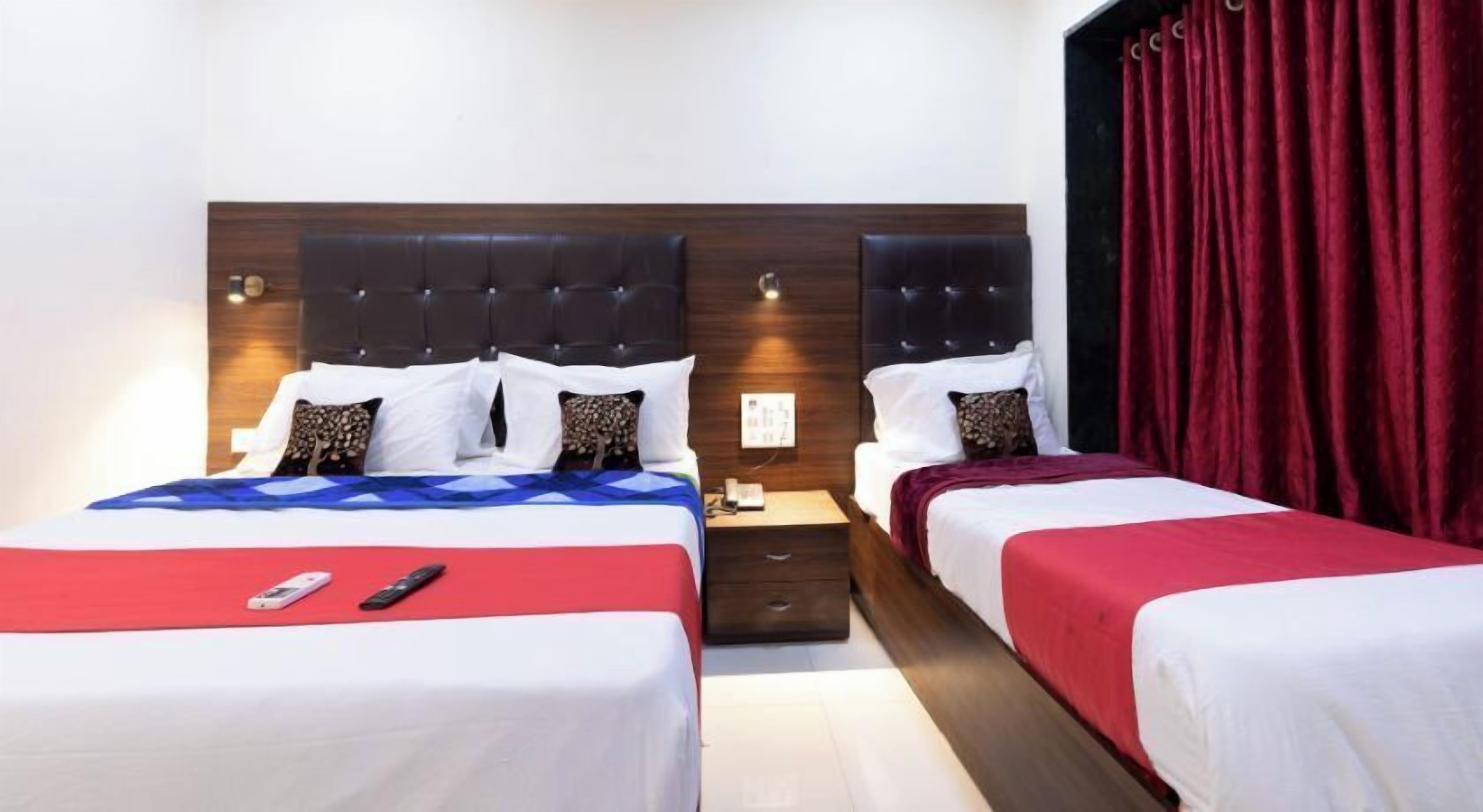A hotel room with two beds, each with a wooden headboard, white bedding, and red accents. There is a nightstand with a phone and a remote control on the left bed.