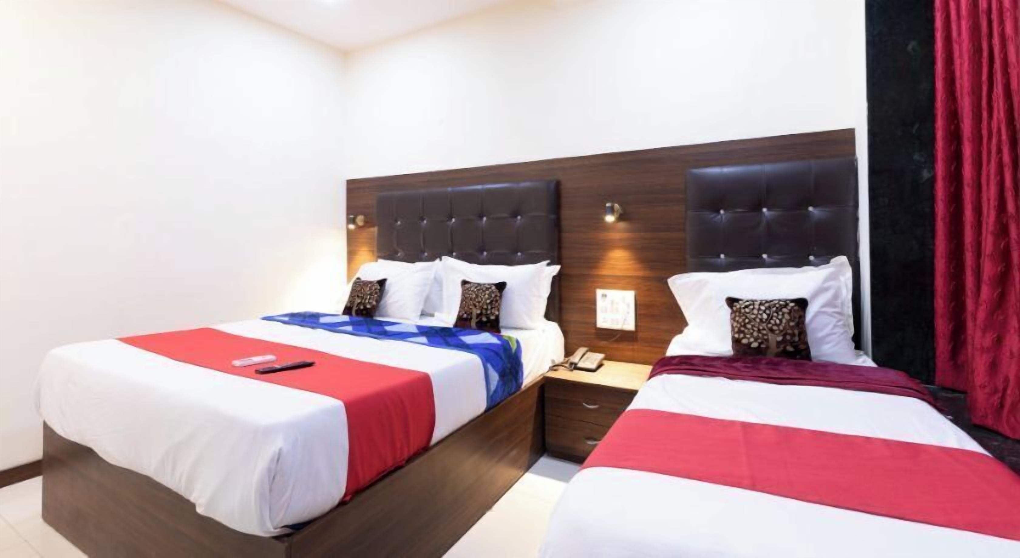 A hotel room with two beds, each with a wooden headboard, white bedding, and red accents. There is a nightstand between the beds with a phone and a lamp.