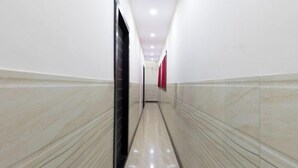 A corridor with white walls and a polished floor, leading to a door at the end. - Hotel Nithyanand (Mumbai)