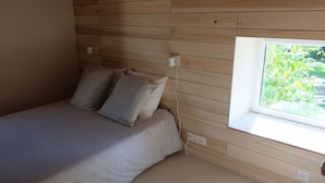 A bedroom with a wooden slat ceiling, a single bed with patterned bedding, a window with a view of greenery, and a power outlet on the wall. - Le Clos de la Ferdière - charming gîte near Cluny (Navour-sur-Grosne)
