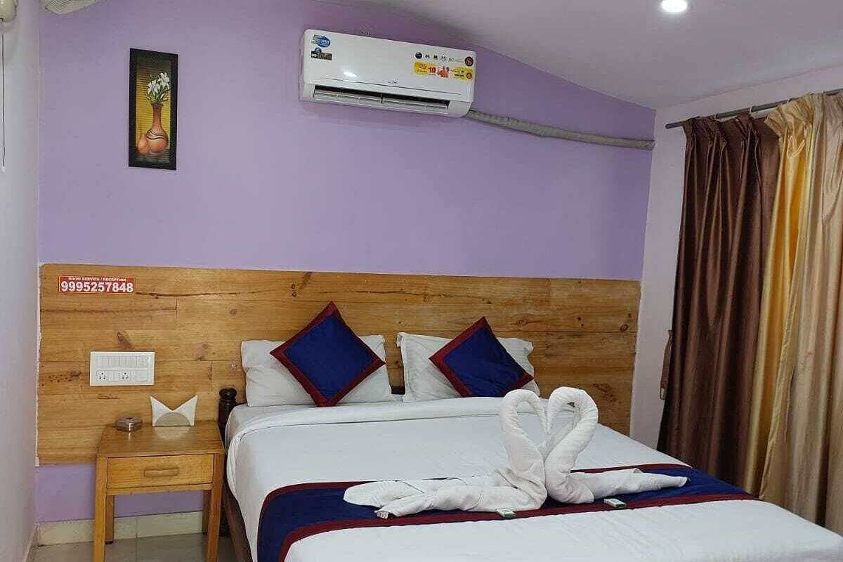 A hotel room with a wooden bed, a nightstand, an air conditioning unit, and a ceiling fan.
