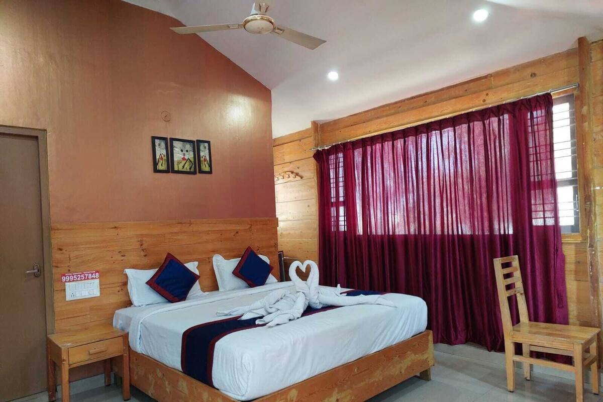 A wooden-framed bed with white bedding and decorative pillows, a ceiling fan, and a window with red curtains.