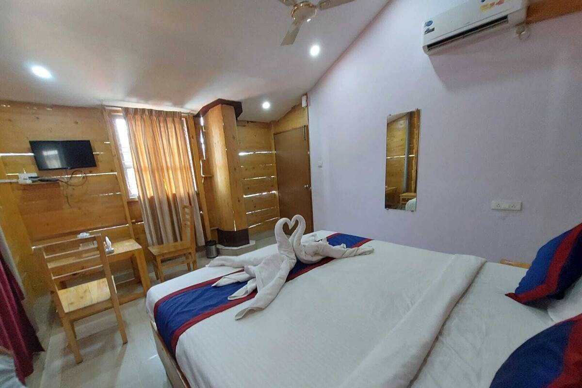 A hotel room with a bed, a desk, a chair, a TV, and an air conditioning unit.
