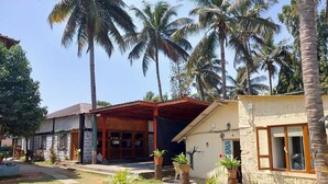 A resort with multiple buildings, including a restaurant and a guesthouse, surrounded by palm trees and potted plants. - Yogi Golden Resort (Mysore)