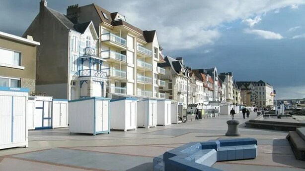 Een kustpromenade met meer verdiepingen tellende gebouwen, waarvan sommigen balkons hebben, onder een heldere lucht.