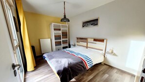 Een slaapkamer met een bed, houten vloeren, een kledingkast, een nachtkastje en een hanglamp.