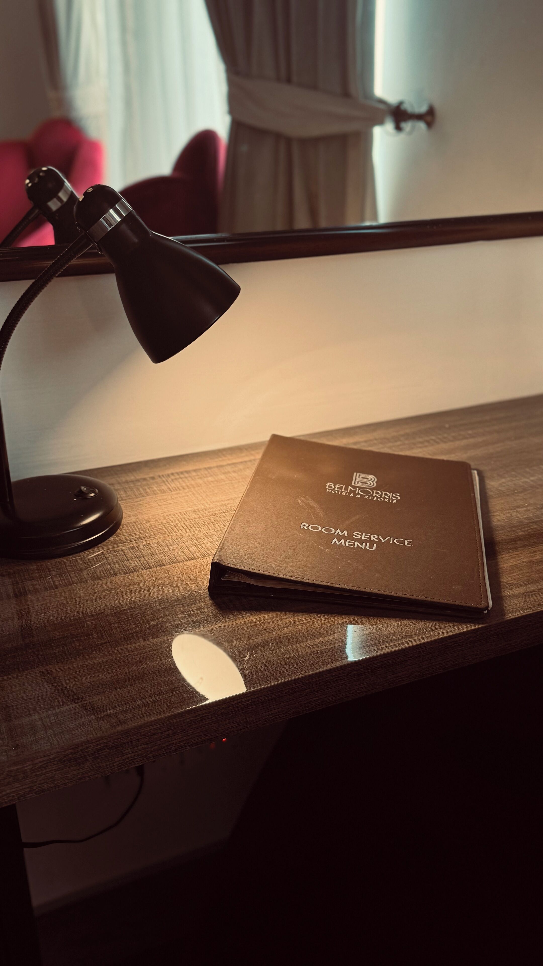Een bureau met een zwarte bureaulamp, een bruin menukaartje en een wit voorwerp op een houten oppervlak.