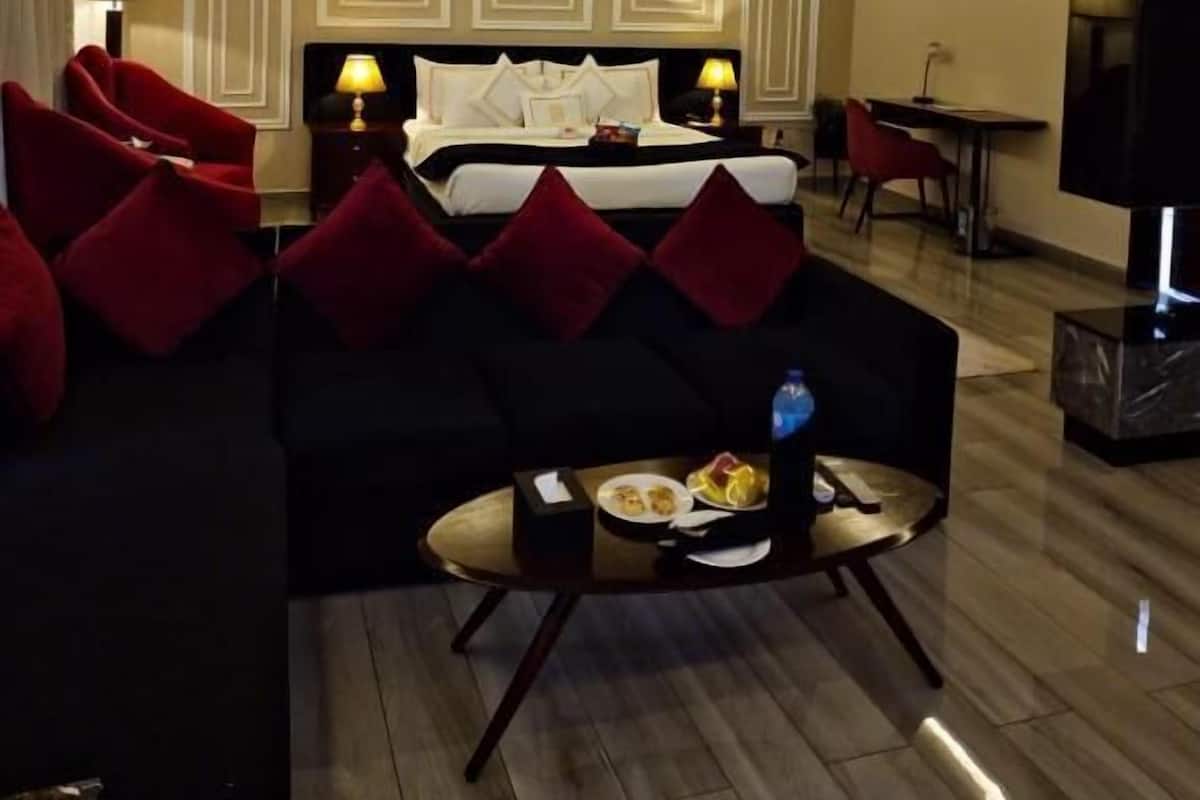 A hotel room with a bed, a sofa, a dining table, and a TV.