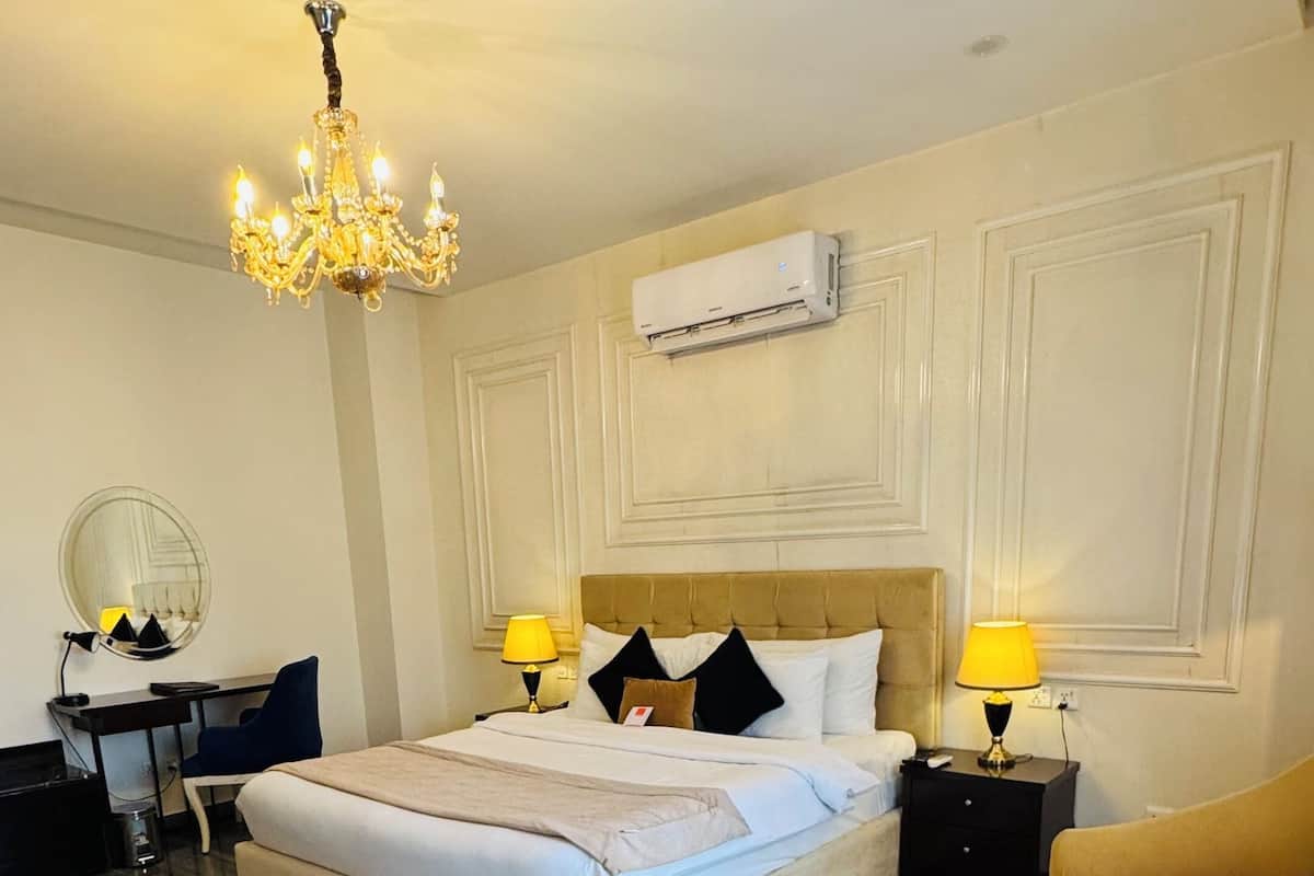 A bedroom with a bed, a desk, a chair, a sofa, a chandelier, and an air conditioning unit.