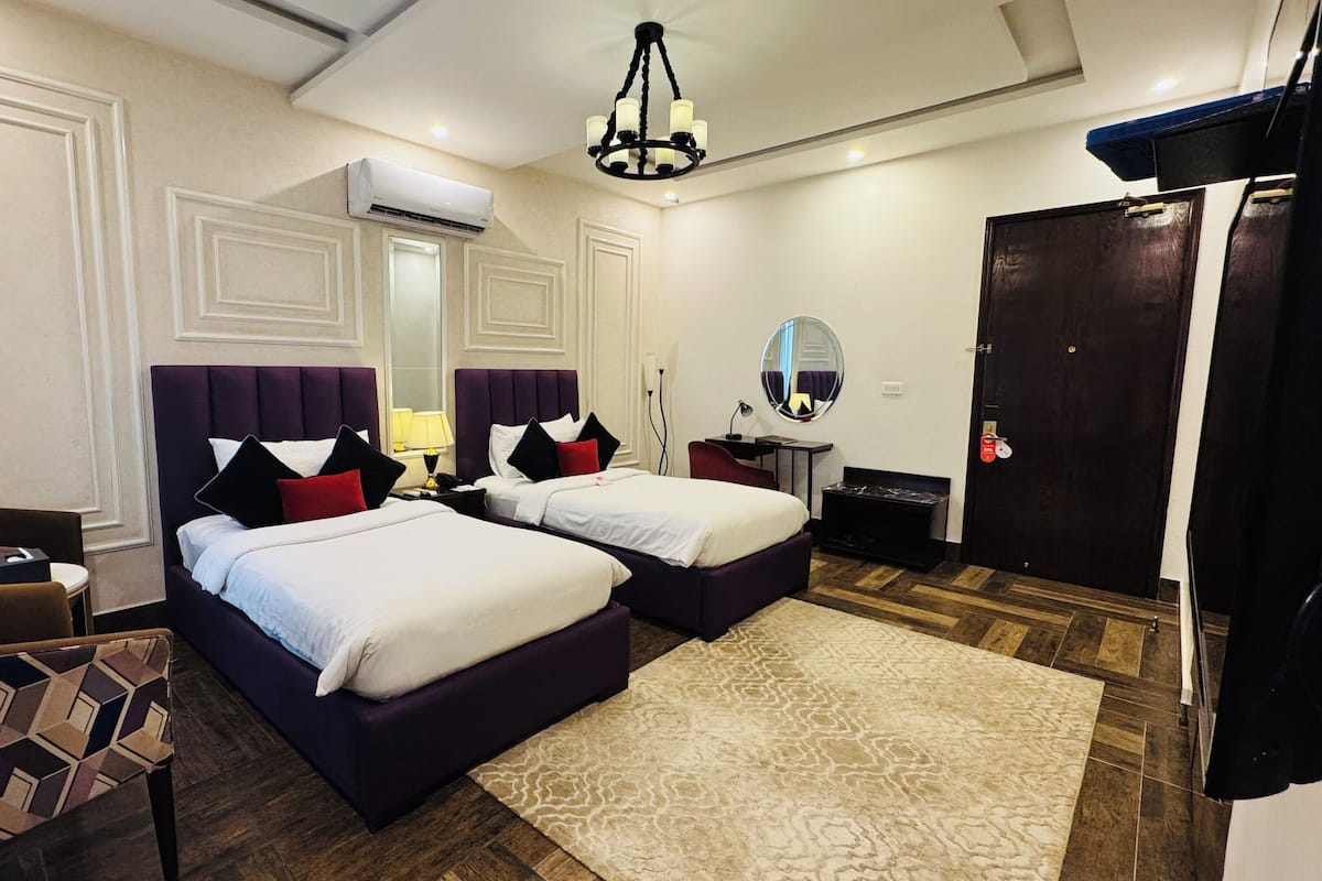 A hotel room with two beds, a desk, a chair, a mirror, and a wardrobe.