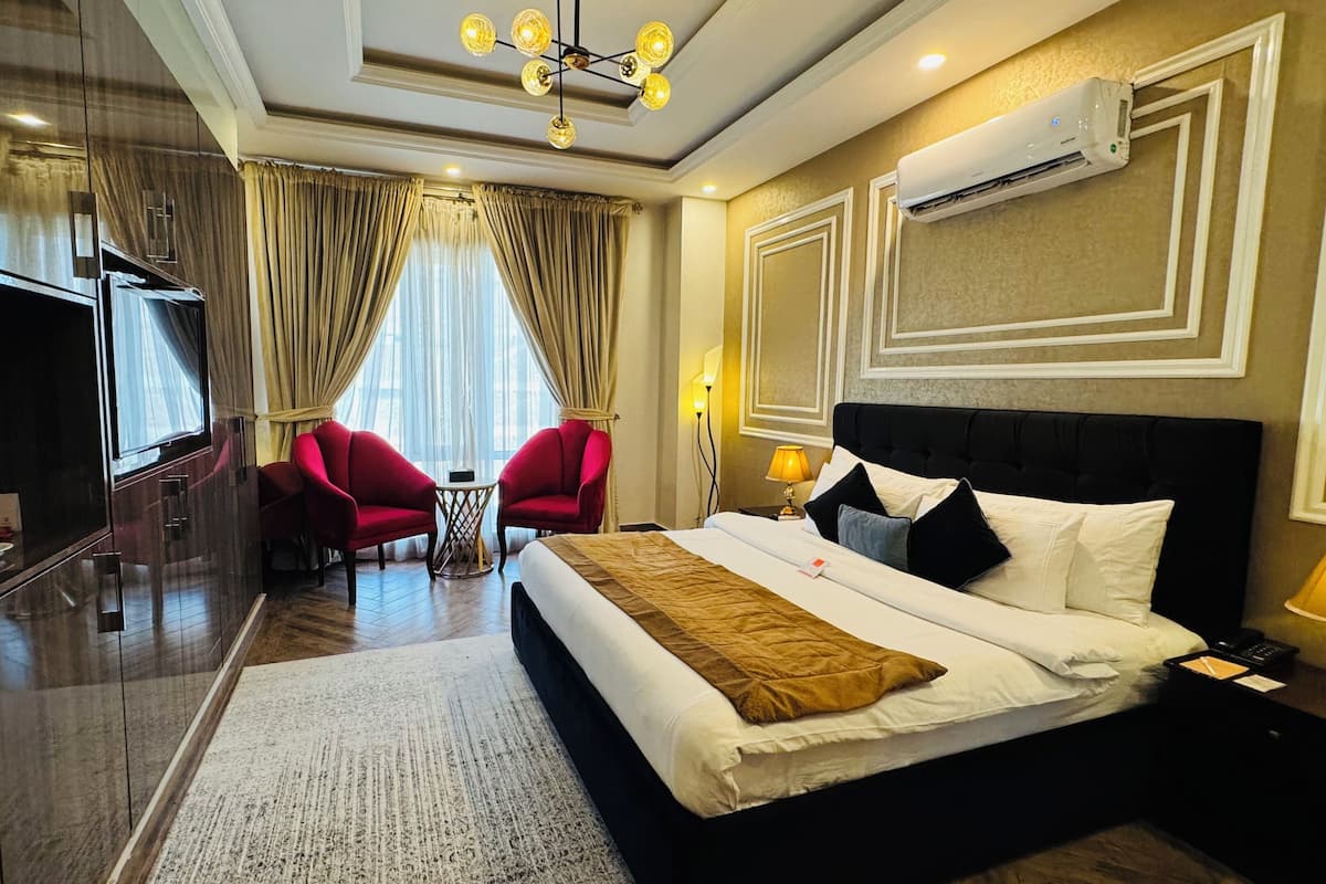 A hotel room with a large bed, two red armchairs, a small table, and a TV.
