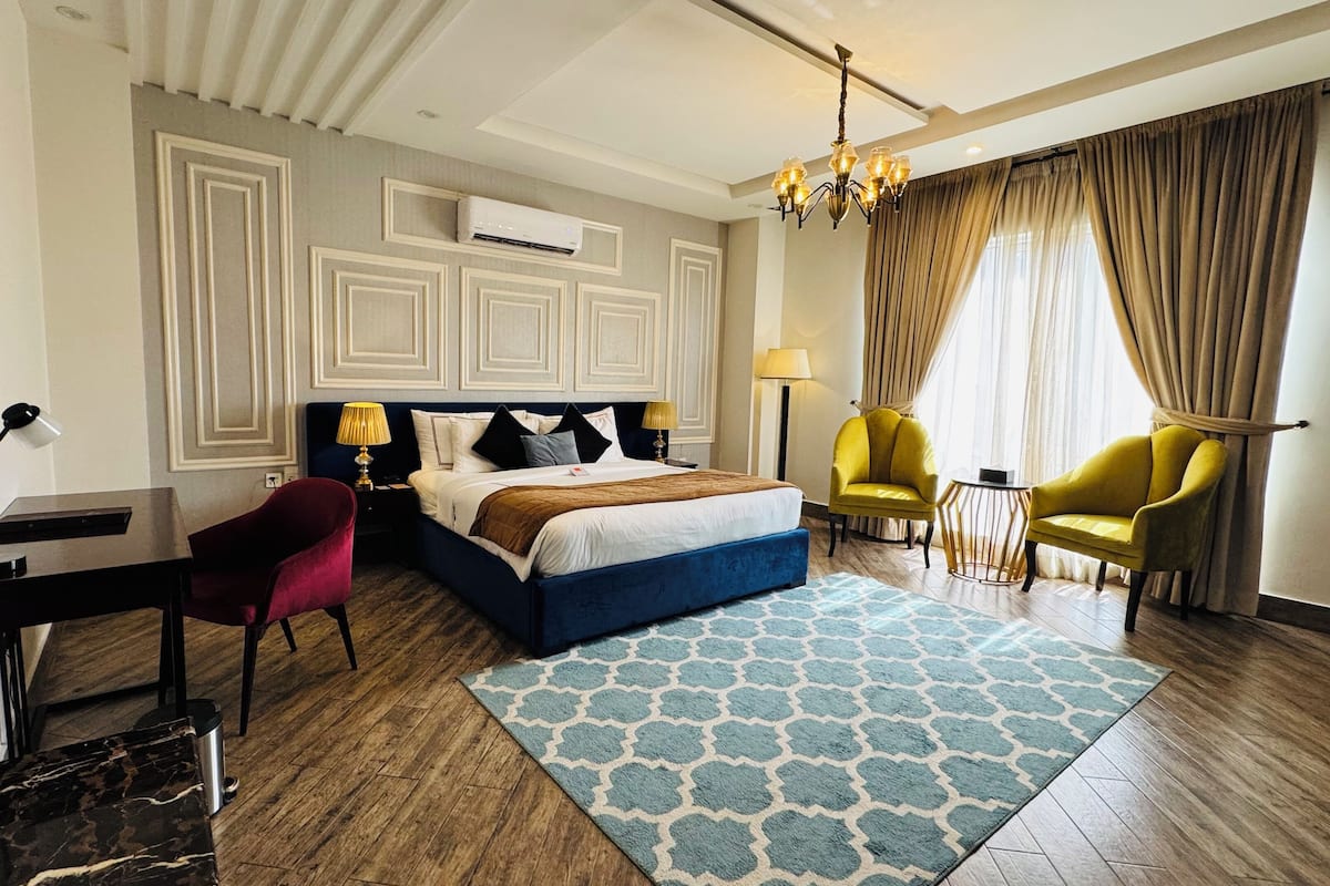 A hotel room with a bed, desk, chairs, and a chandelier.